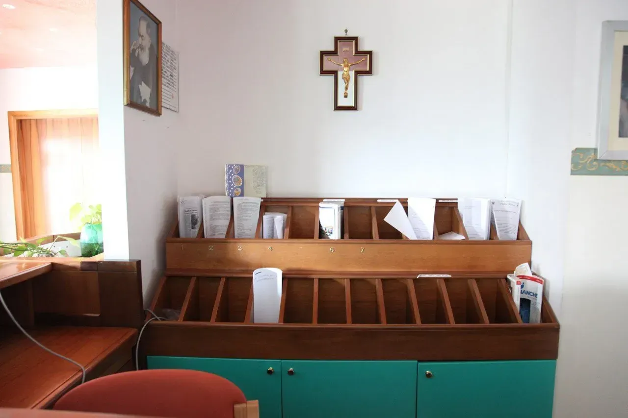 Interno con un leggio in legno per i libri dei canti religiosi, una Bibbia, una croce sul muro e armadietti verdi.