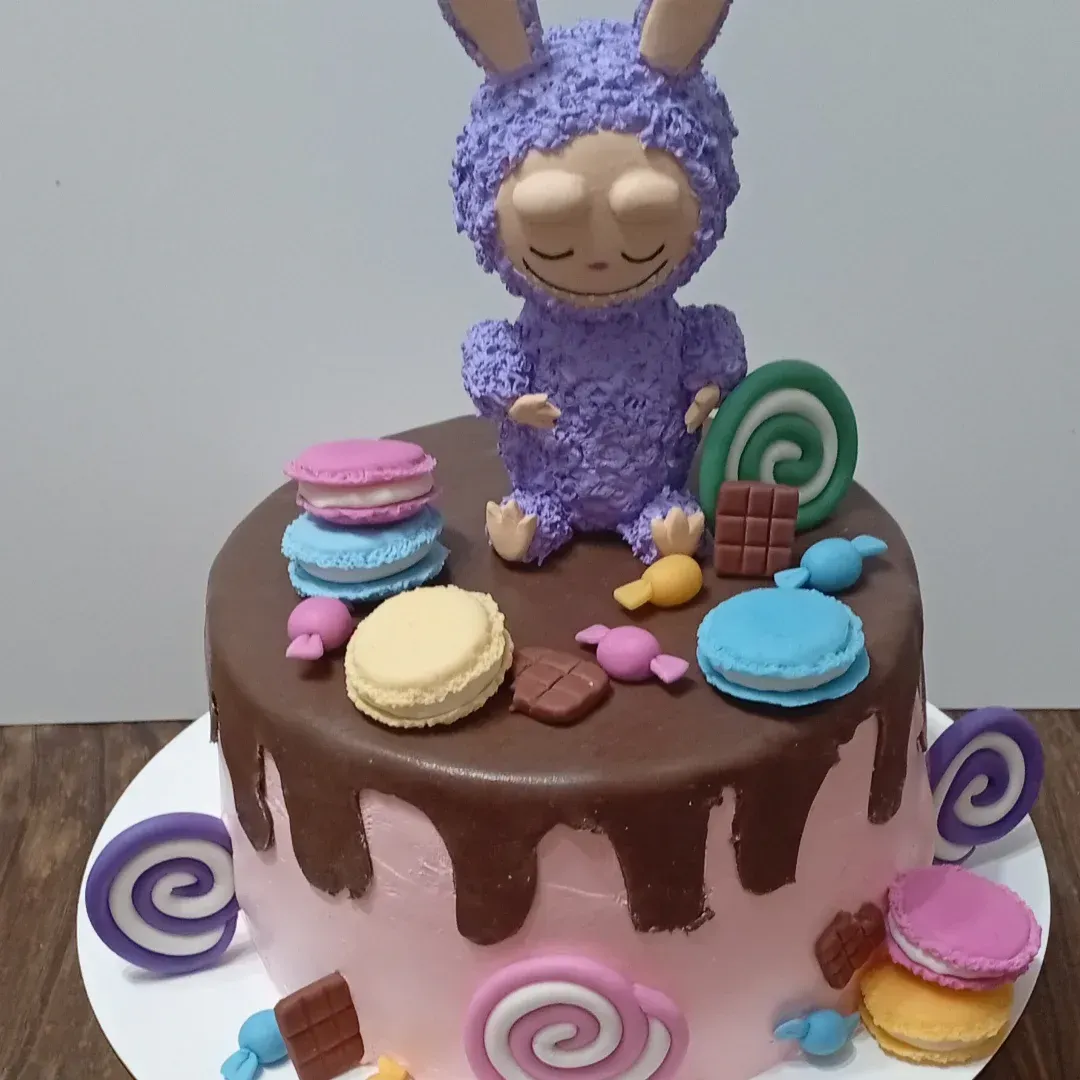 Pastel con criatura morada y dulces, gotas de chocolate sobre glaseado rosa.