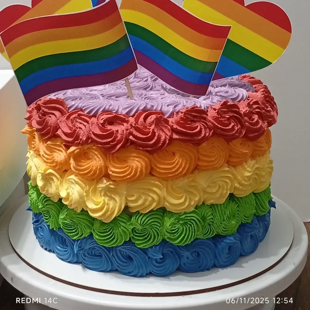 Pastel con capas de arcoíris y banderas del Orgullo en la parte superior, decorado con remolinos de glaseado de colores.