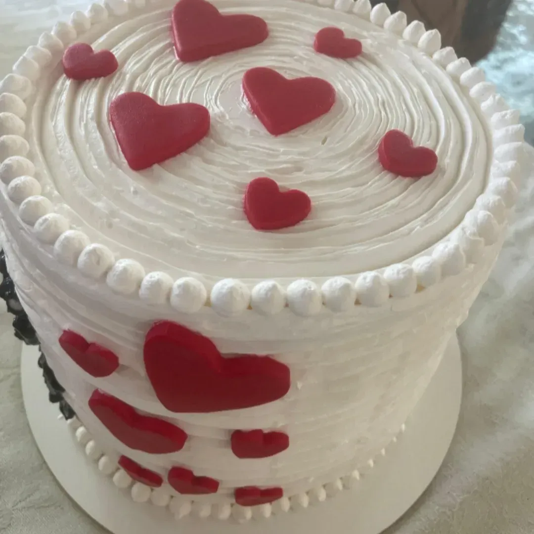 Pastel blanco decorado con corazones rojos, glaseado de crema de mantequilla y borde con manga pastelera.