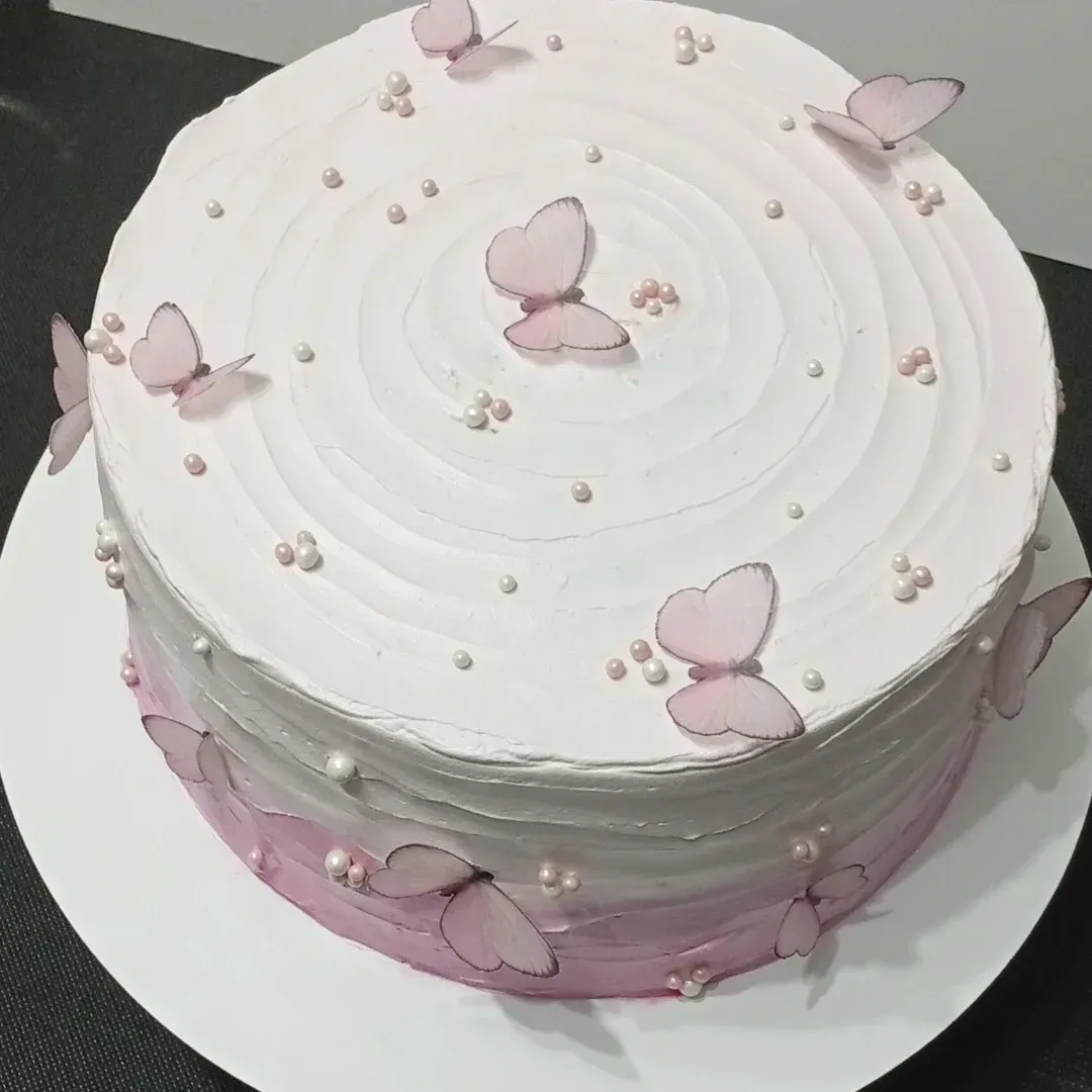 Pastel rosa y blanco decorado con mariposas rosas y perlas, sobre un plato blanco.