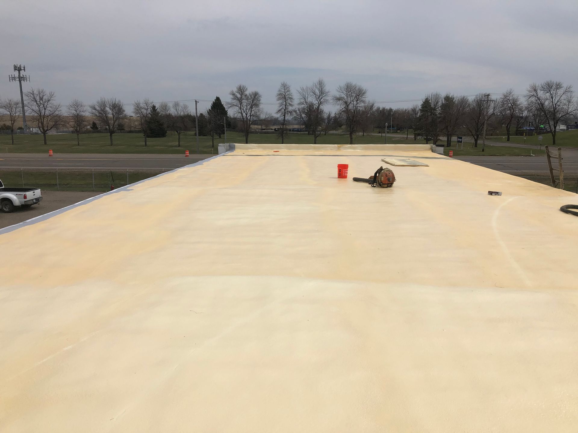 Roof with light-colored coating, a person working, and tools present.
