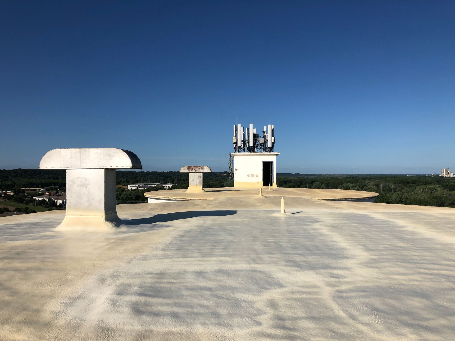 Rooftop view of communication equipment and structures against a clear blue sky.
