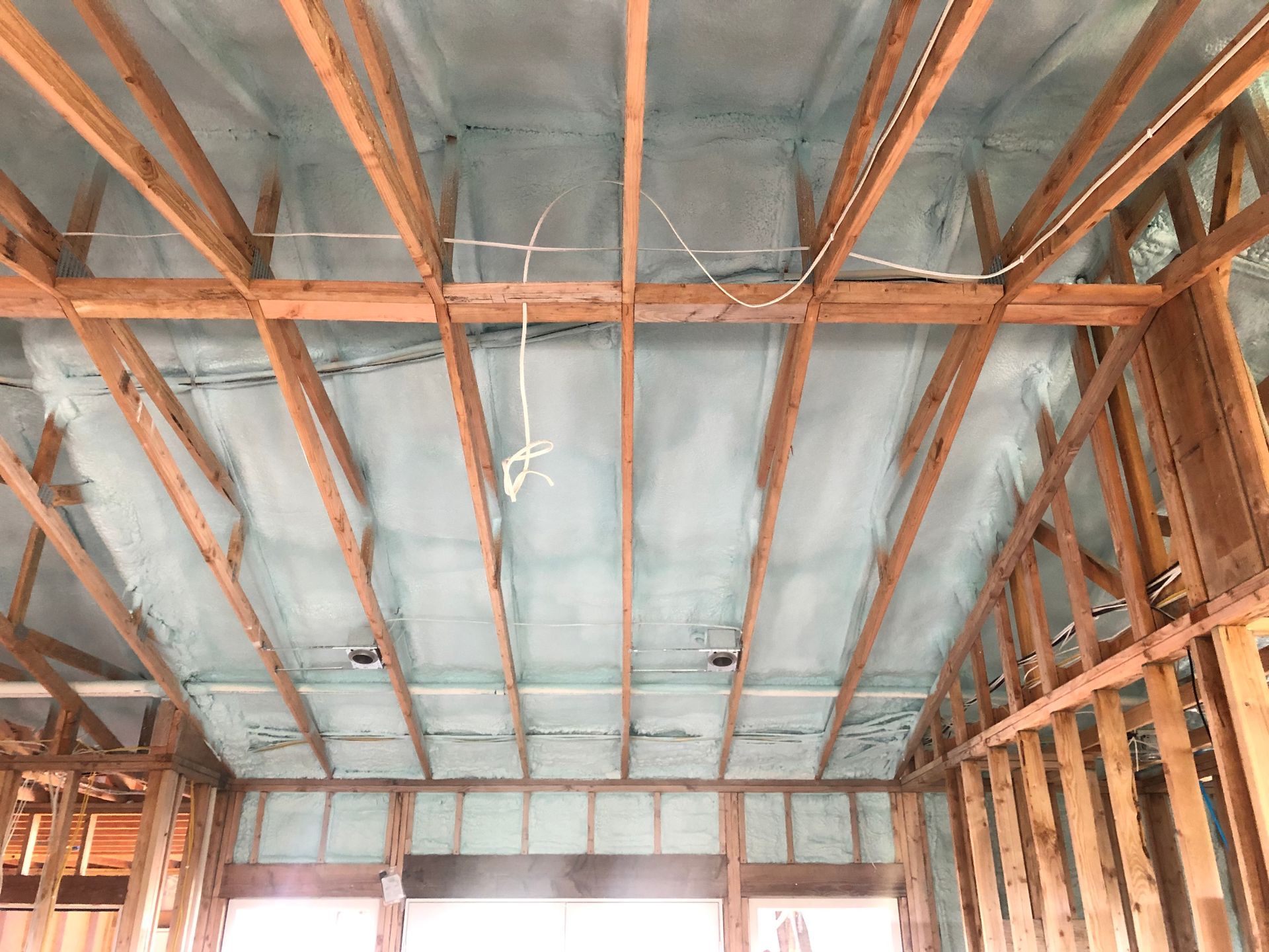 Interior view of a building under construction, featuring wooden framing and spray foam insulation on the ceiling.