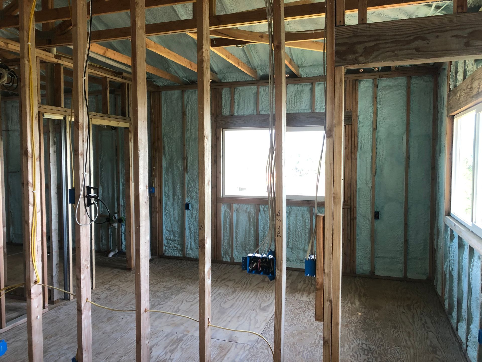 Interior of a building under construction, wooden frames with spray foam insulation, windows visible.