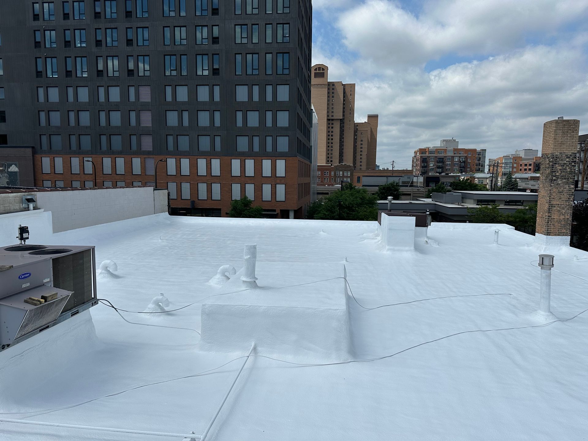 White rooftop with various vents, against backdrop of city buildings and cloudy sky.