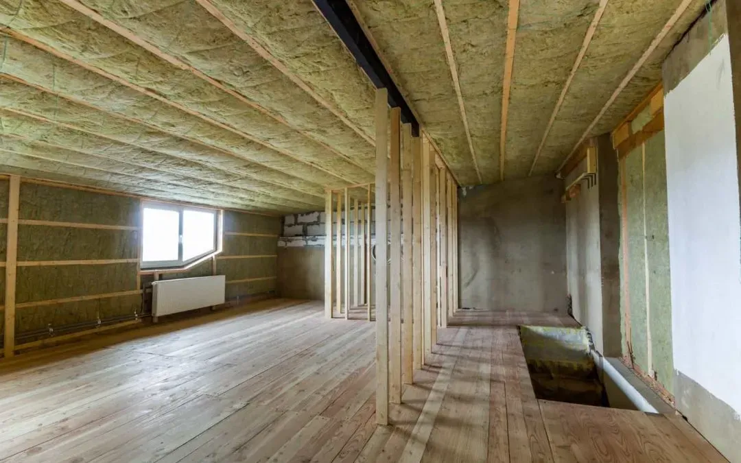 Partially finished attic with exposed insulation, wooden framing, and a small window.
