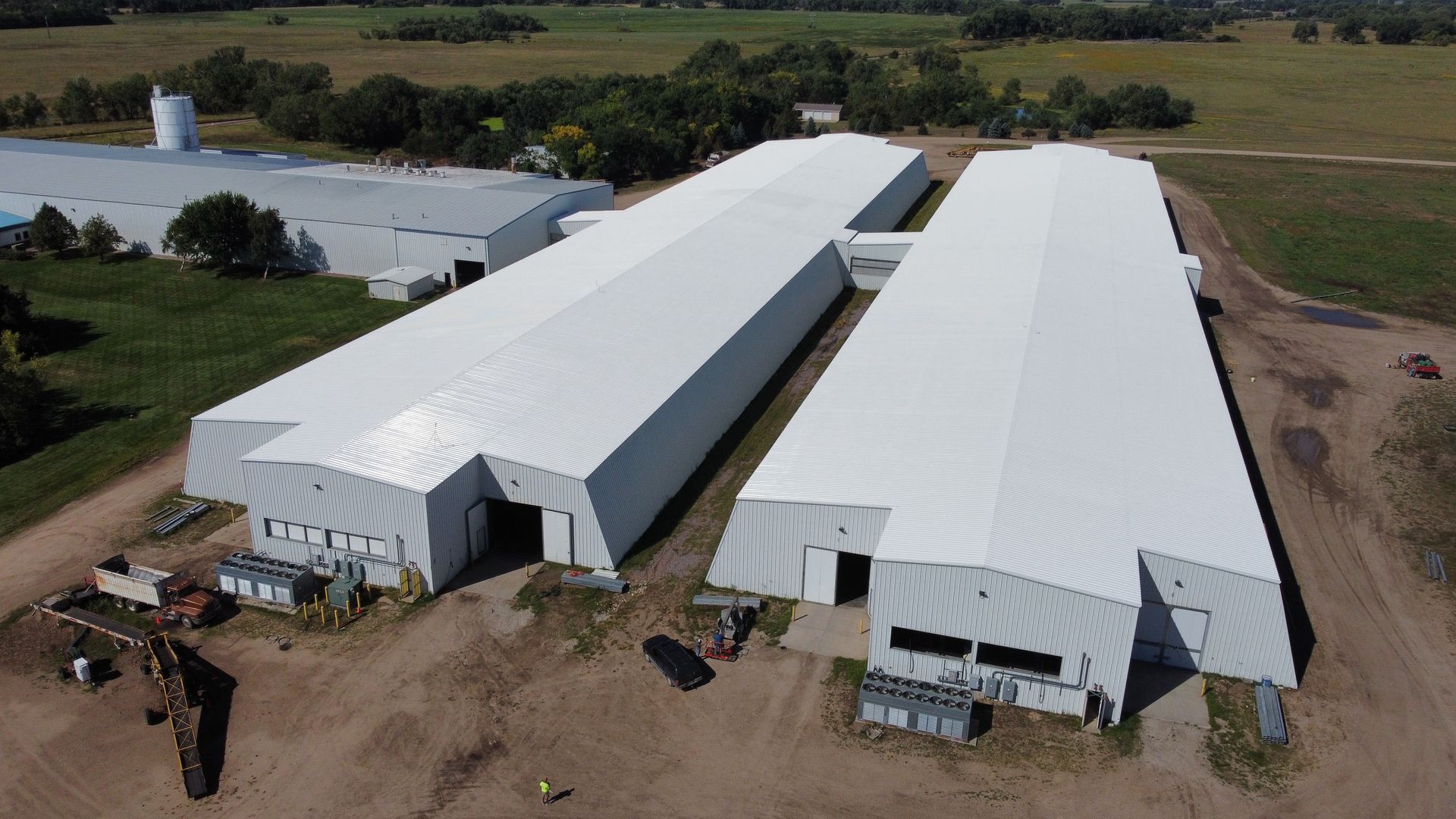Aerial view of two large, white industrial buildings with open entryways on a rural property.