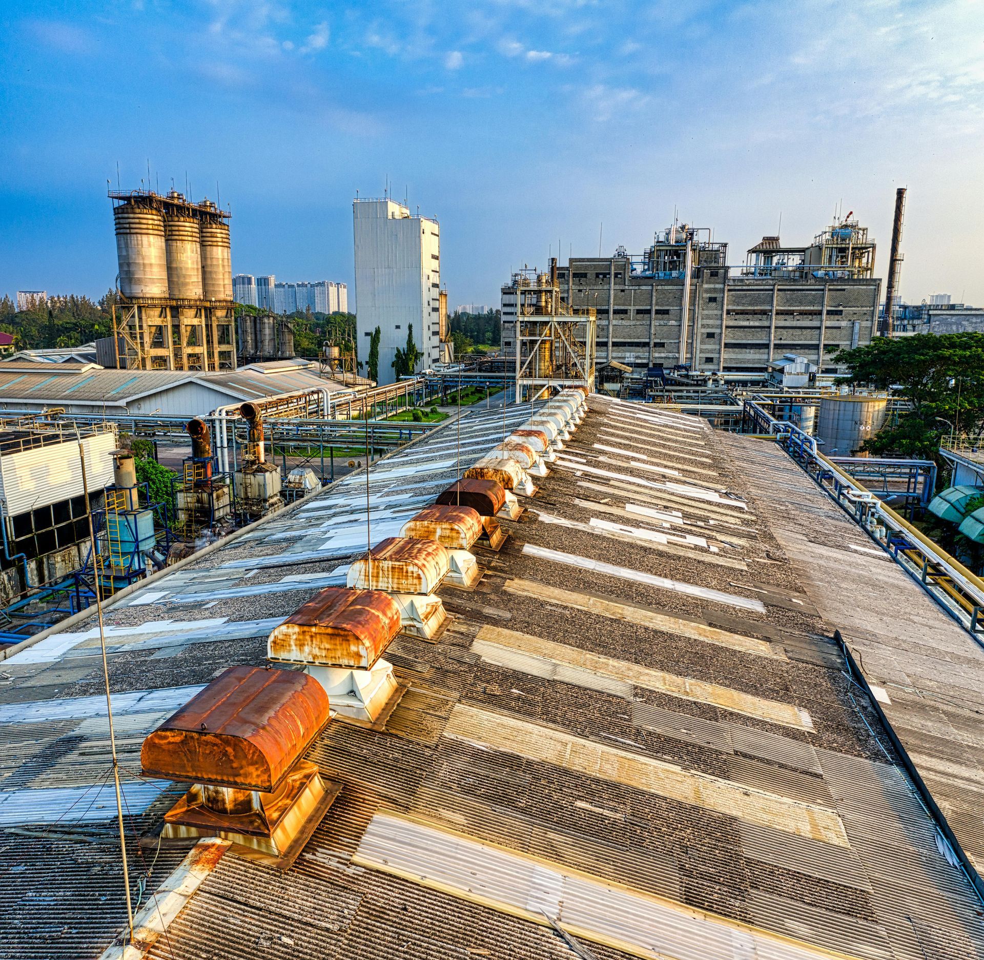 Industrial rooftop with corrugated metal roofs, rusted vents, and factory buildings in the background.