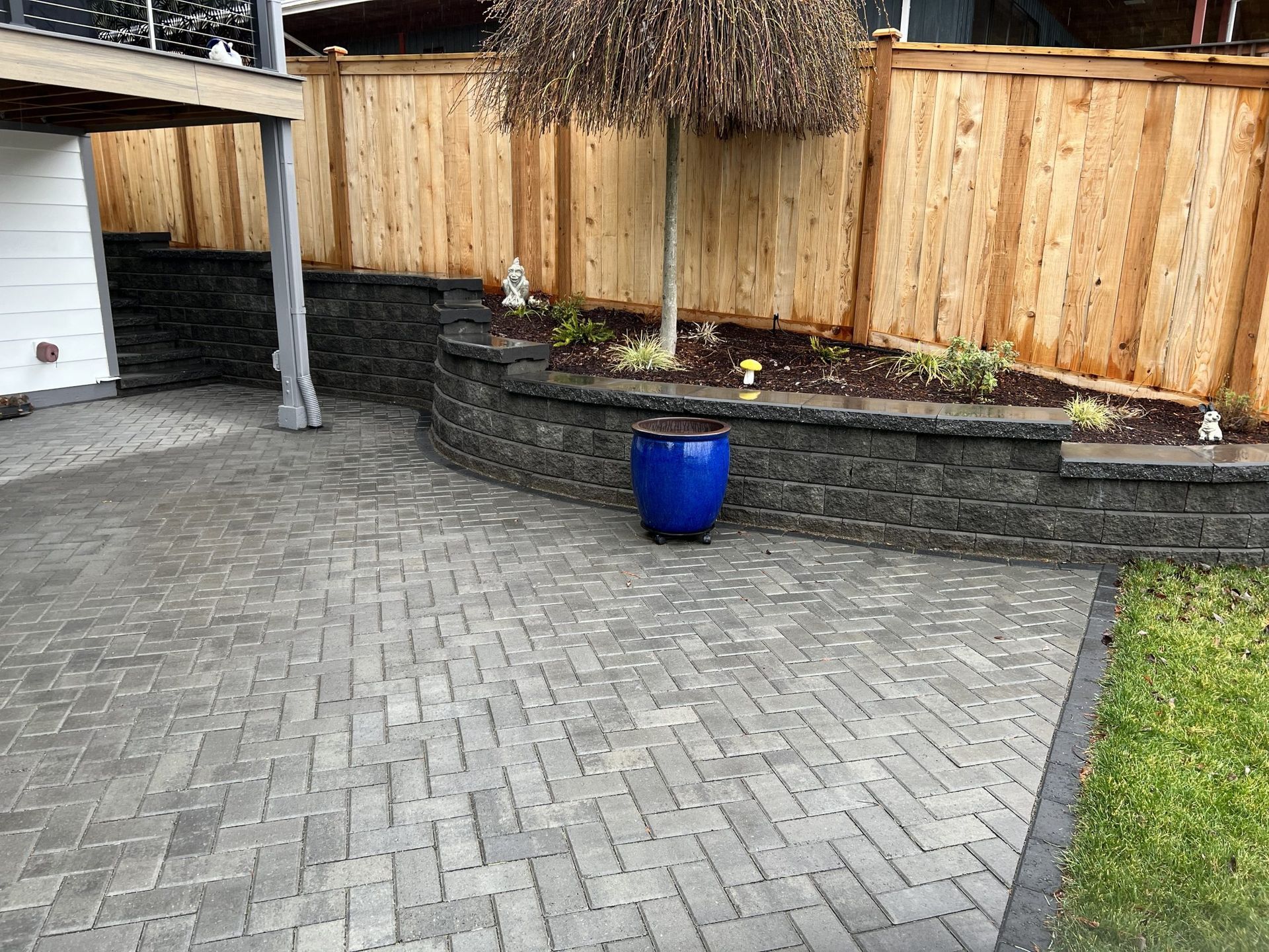 A blue pot is sitting on a brick patio next to a wooden fence.