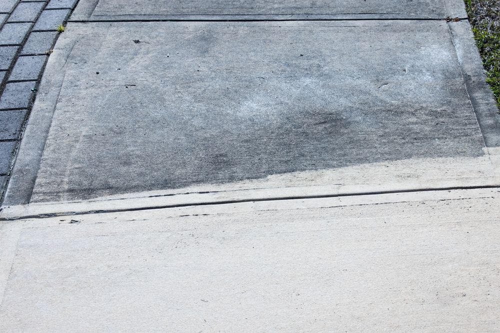 A gray concrete sidewalk transitions from weathered, dark stone to a newer, lighter, brushed concrete section.