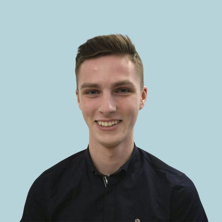 Young man smiling, wearing a dark blue shirt, against a light blue background.
