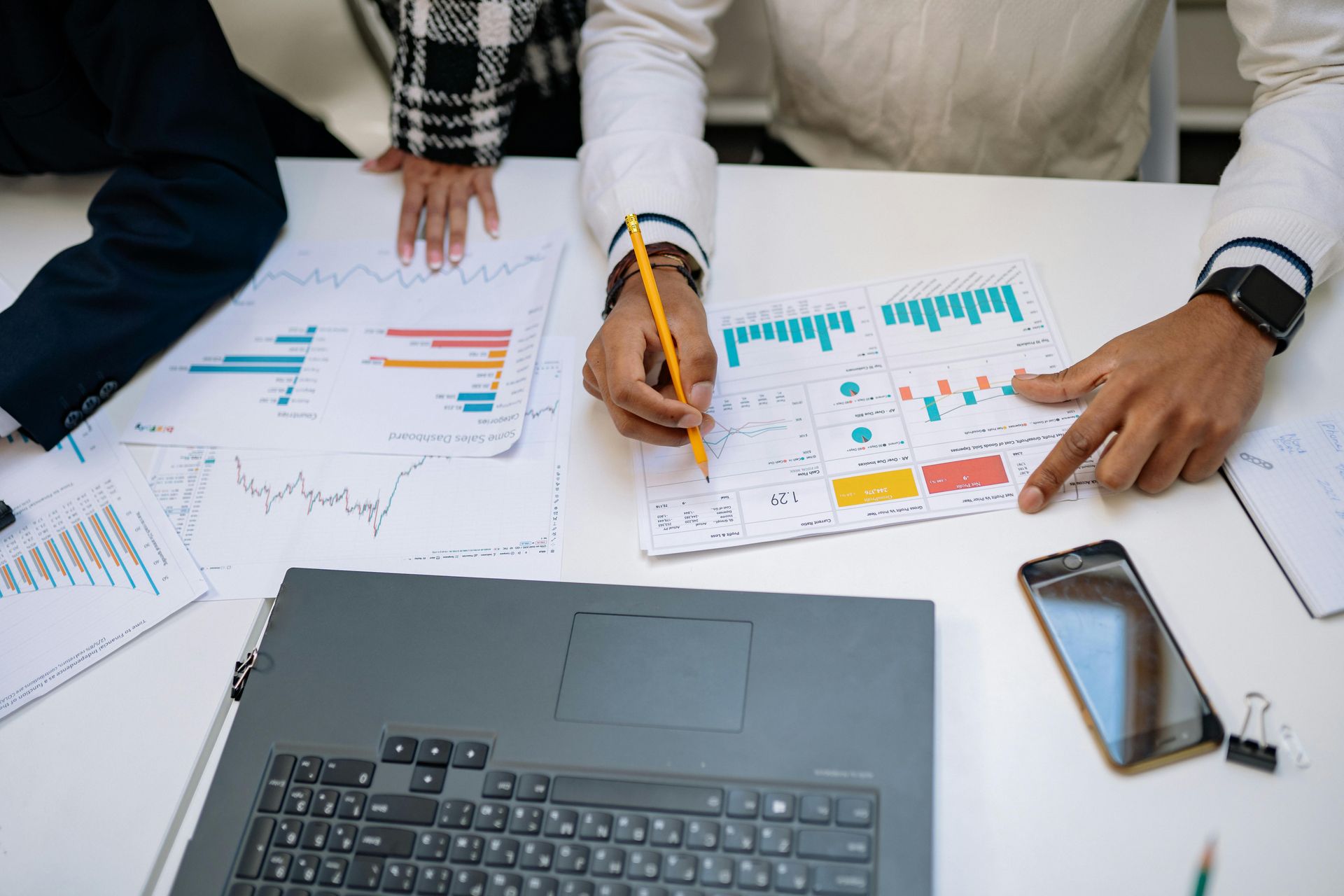 Team reviewing printed charts at a desk with a laptop, smartphone, and financial graphs