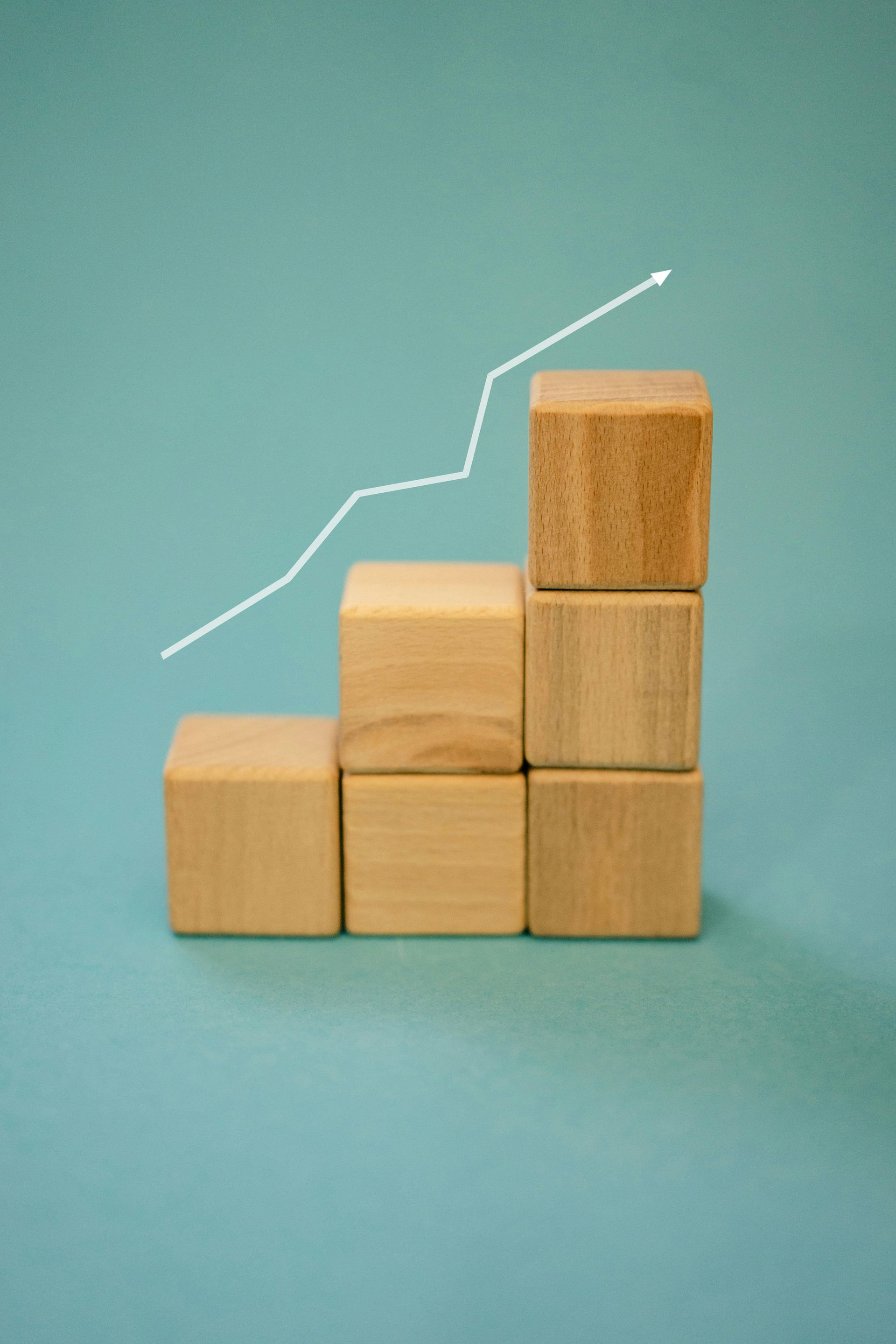 Wooden blocks stacked in a stepped chart with a rising white line on a teal background