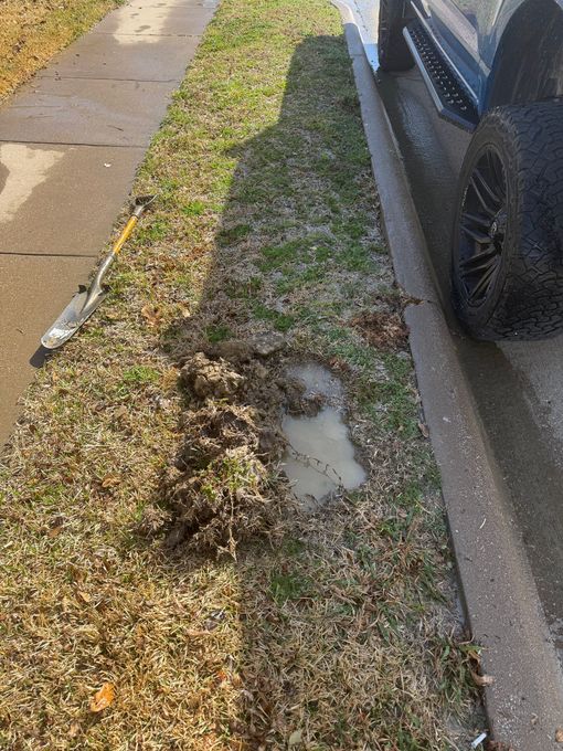 Mud and water pooled on a grassy area next to a sidewalk and parked car.