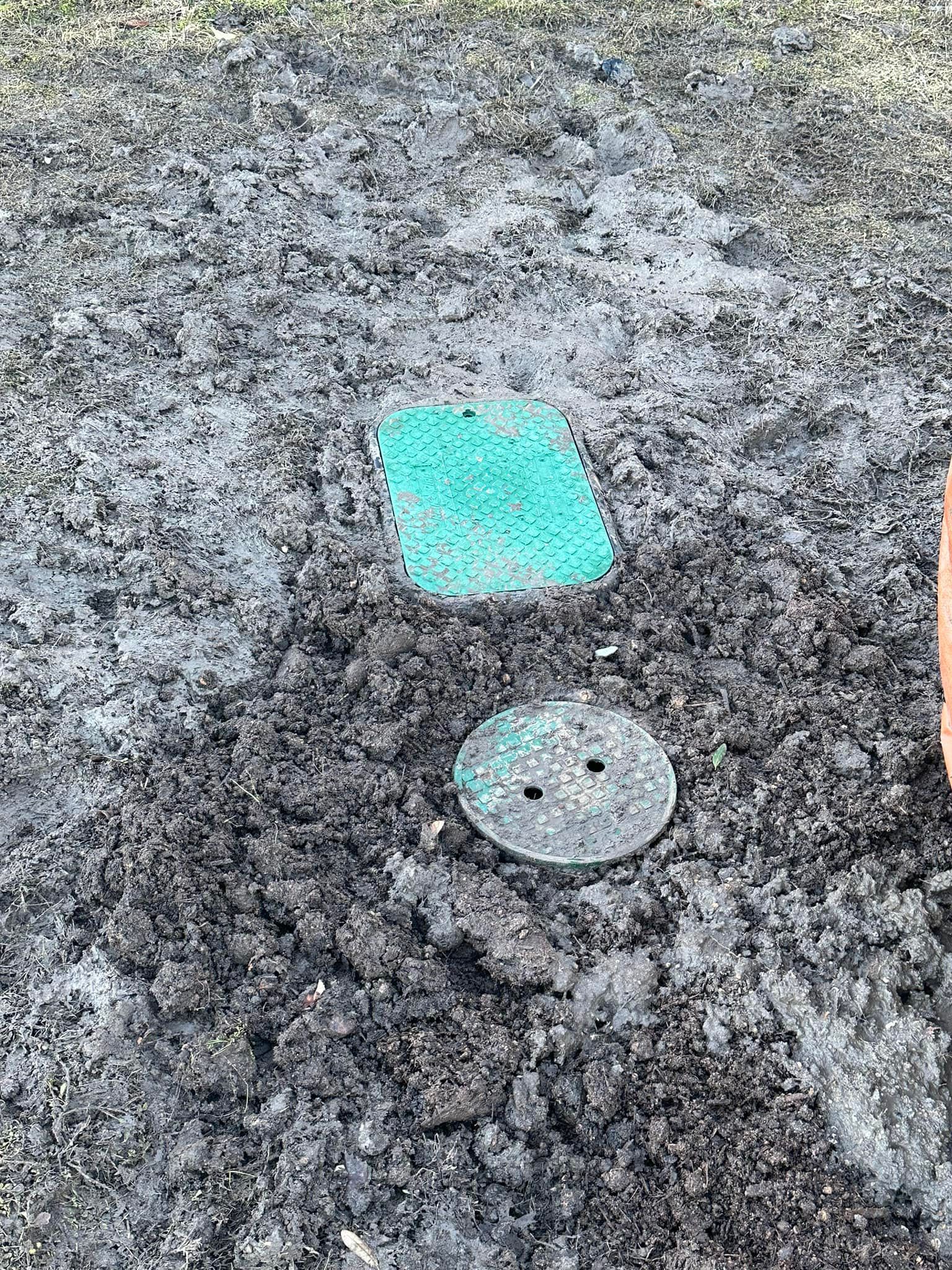 Two circular and square covers in dark soil, one green and one bronze.