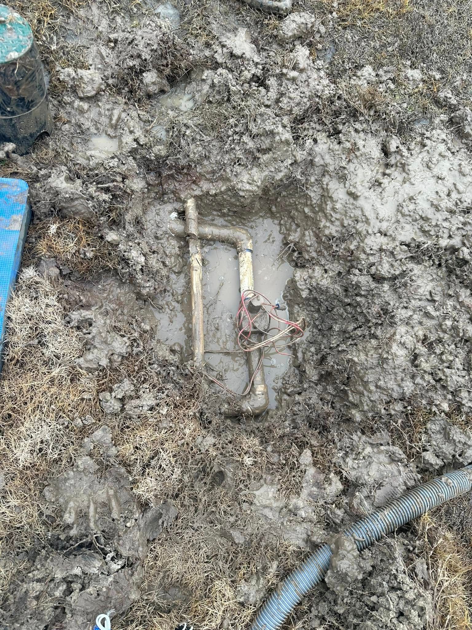 Pipes and valve exposed in muddy ground; part of an irrigation system installation.
