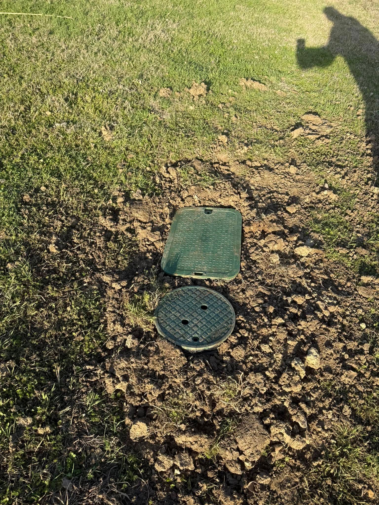 Green sprinkler system control box lids on dirt and grass.