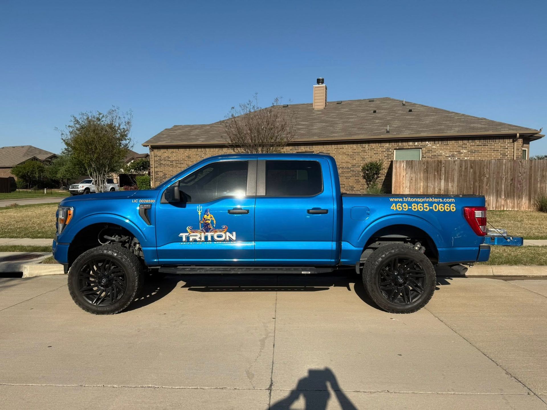 Blue Triton truck parked on a street with a house in the background.