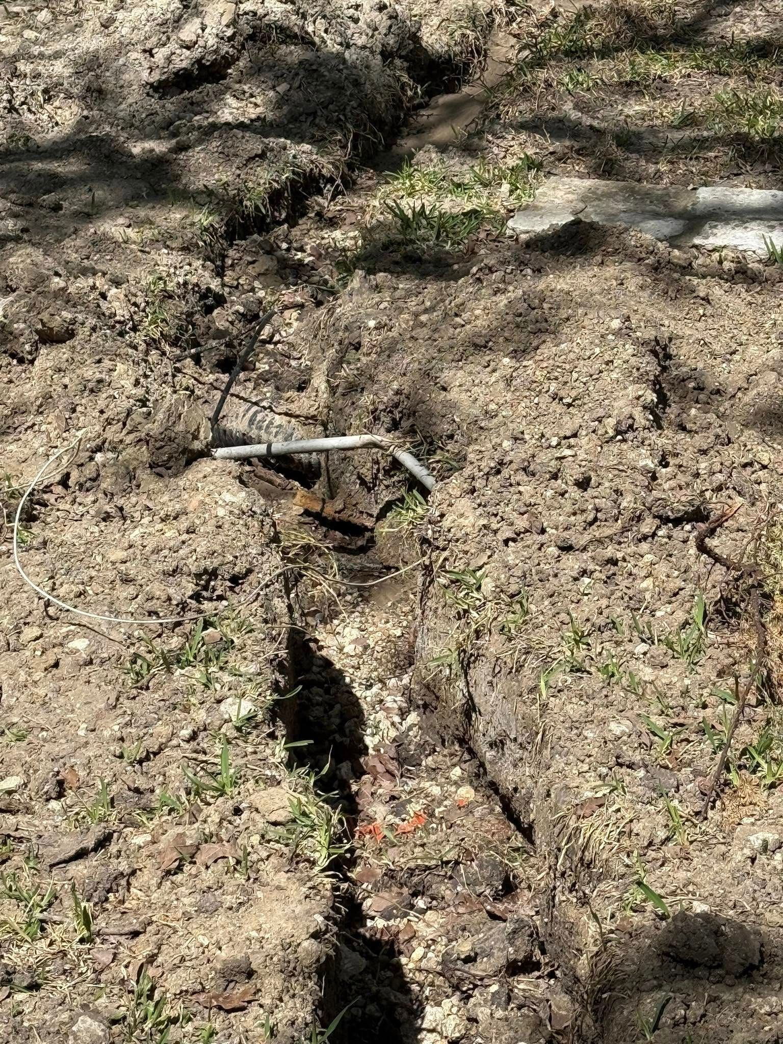 Trench in dirt with irrigation pipe visible. The trench is filled with loose soil, outdoors.