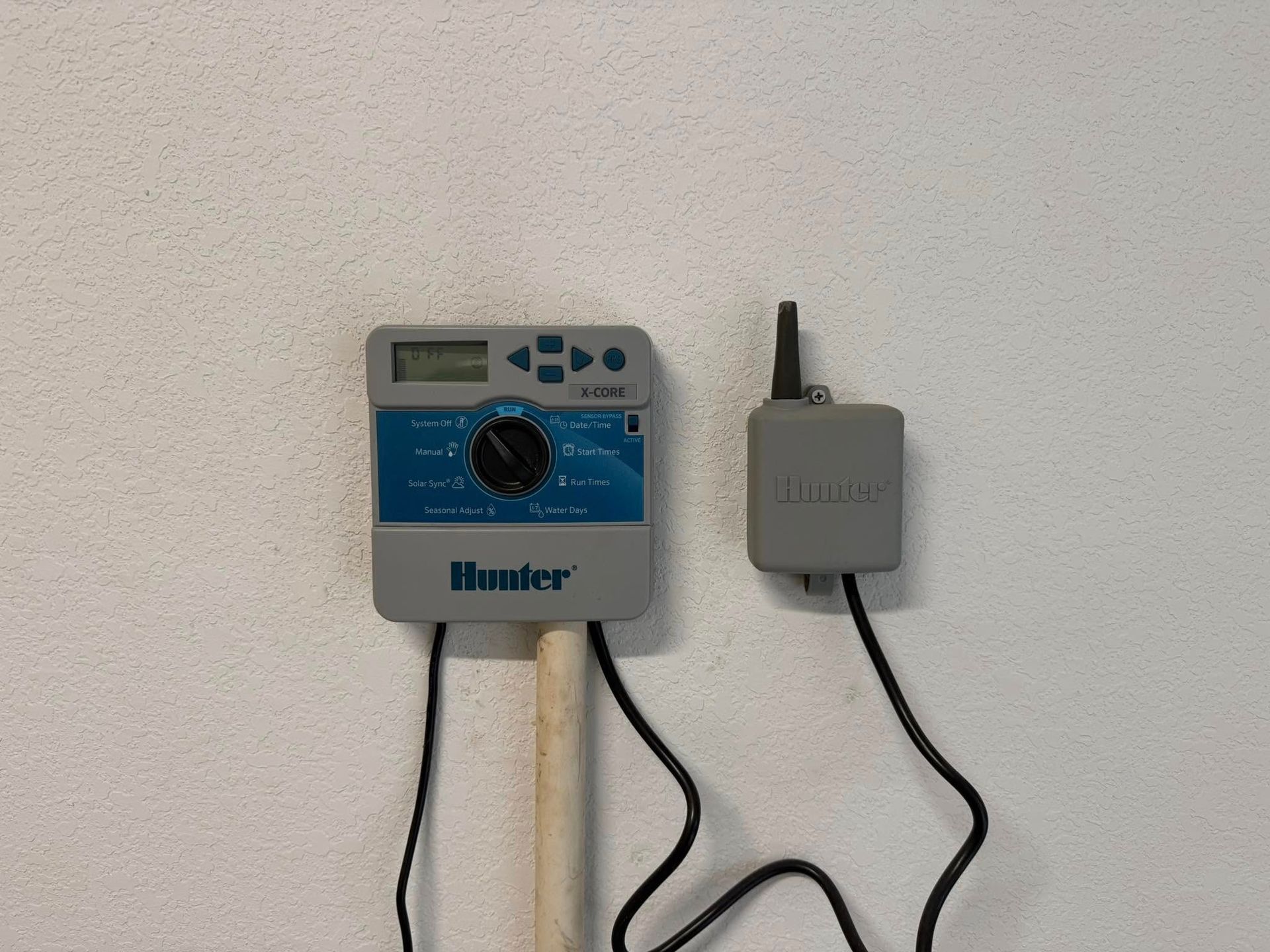 Hunter irrigation timer and receiver mounted on a white wall, connected by black wires.