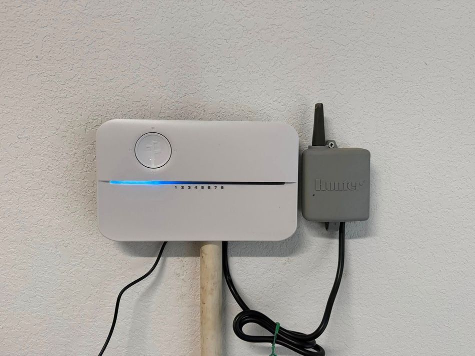 White irrigation control panel and sensor box mounted on a white wall.