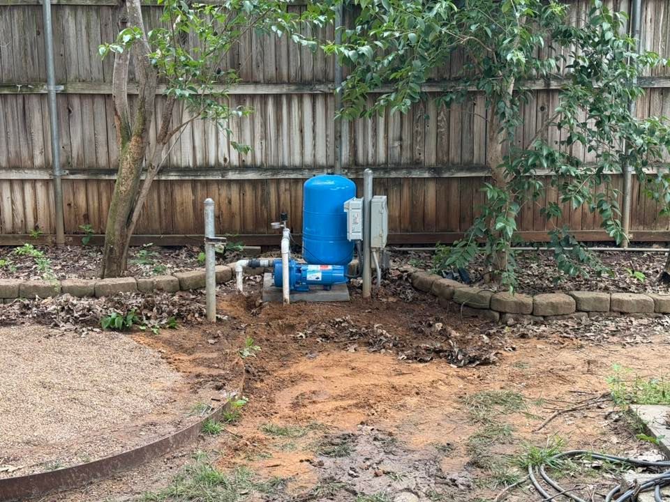 Blue water well tank and pump near a wooden fence and trees, set in a backyard.