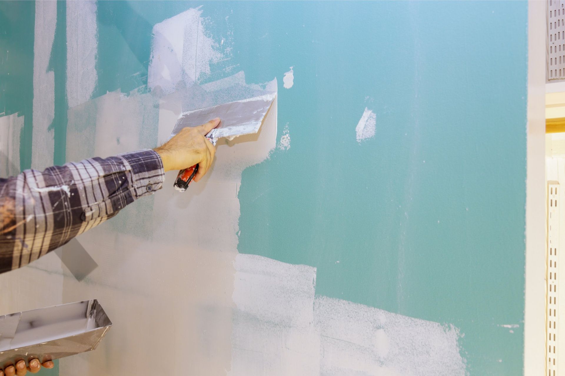 Person applying drywall compound to a blue wall with a trowel.