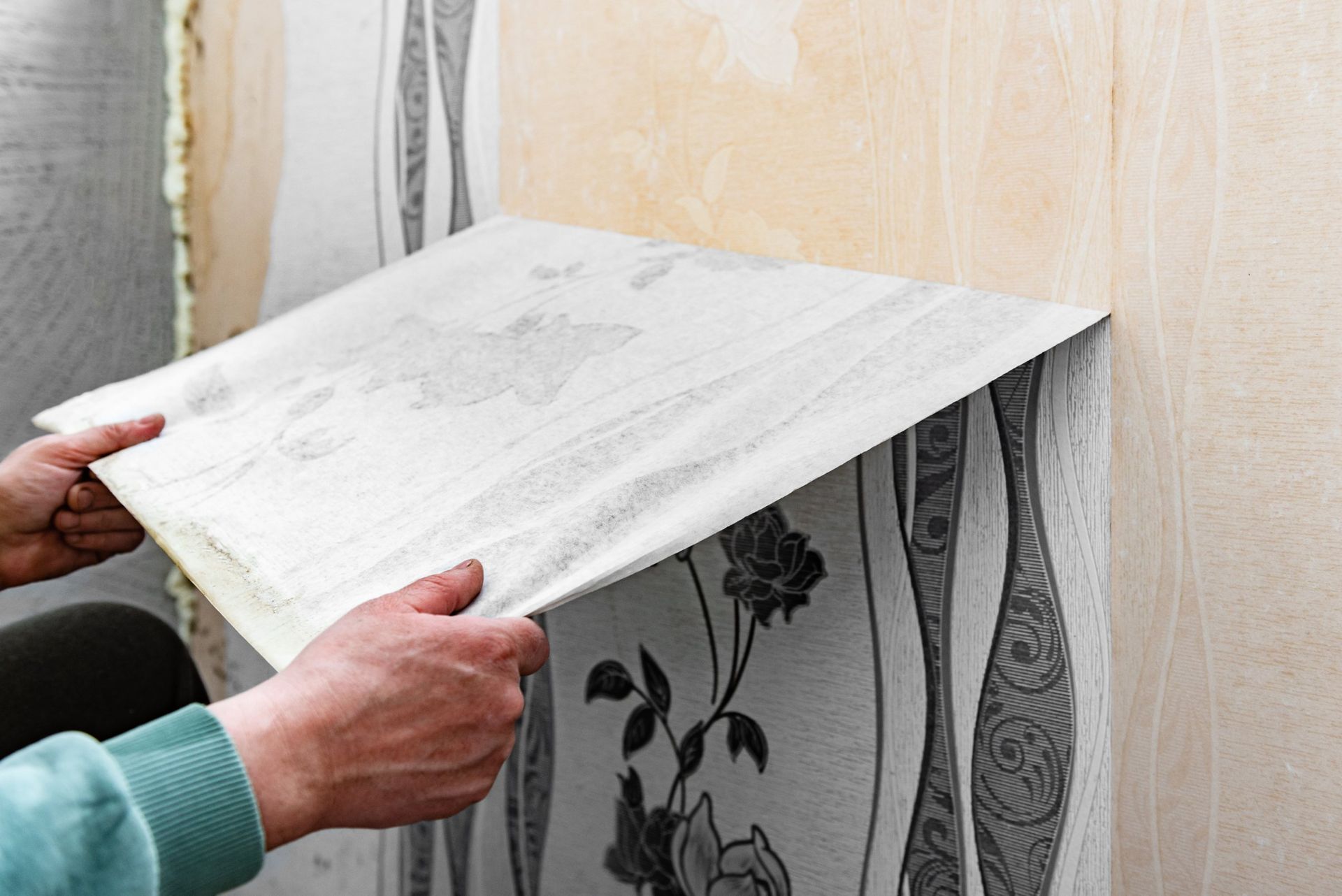 Person placing wallpaper on a wall. Hands holding the sheet. Partially stripped wall in background.