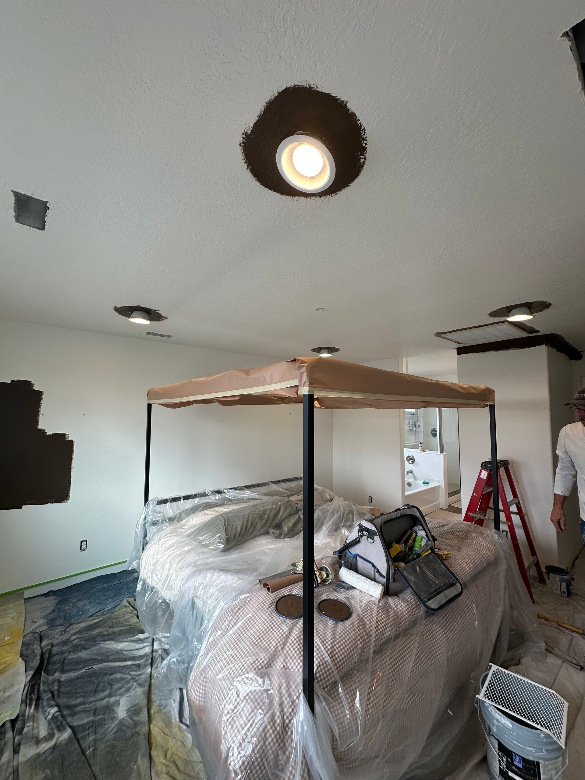 Interior view of a room under renovation, with a bar structure, plastic wrap, and ceiling lights, covered in brown paint.