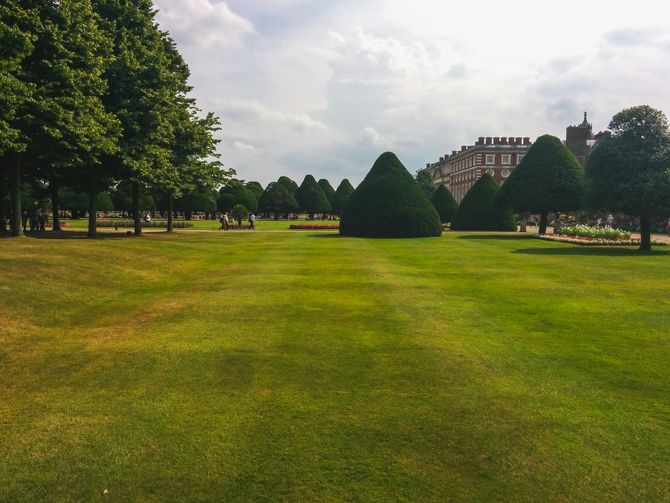 Large green lawn with cone-shaped topiary trees and a brick building.