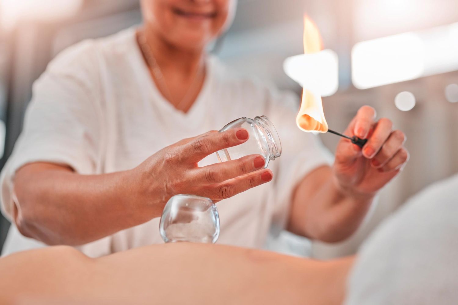 Person pouring liquid into a glass jar while another hand holds a lit match near a flame indoors