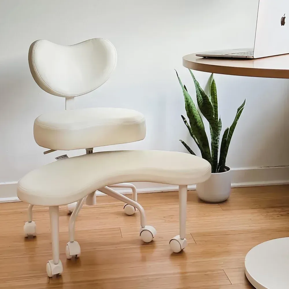Cream ergonomic chair with white frame and wheels beside a potted plant in a bright office corner