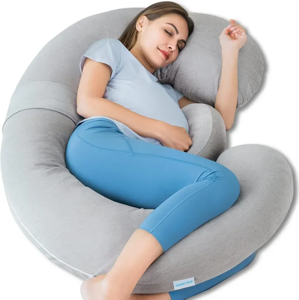 Child sleeping on a gray U-shaped body pillow, curled up in a light blue shirt and pants.