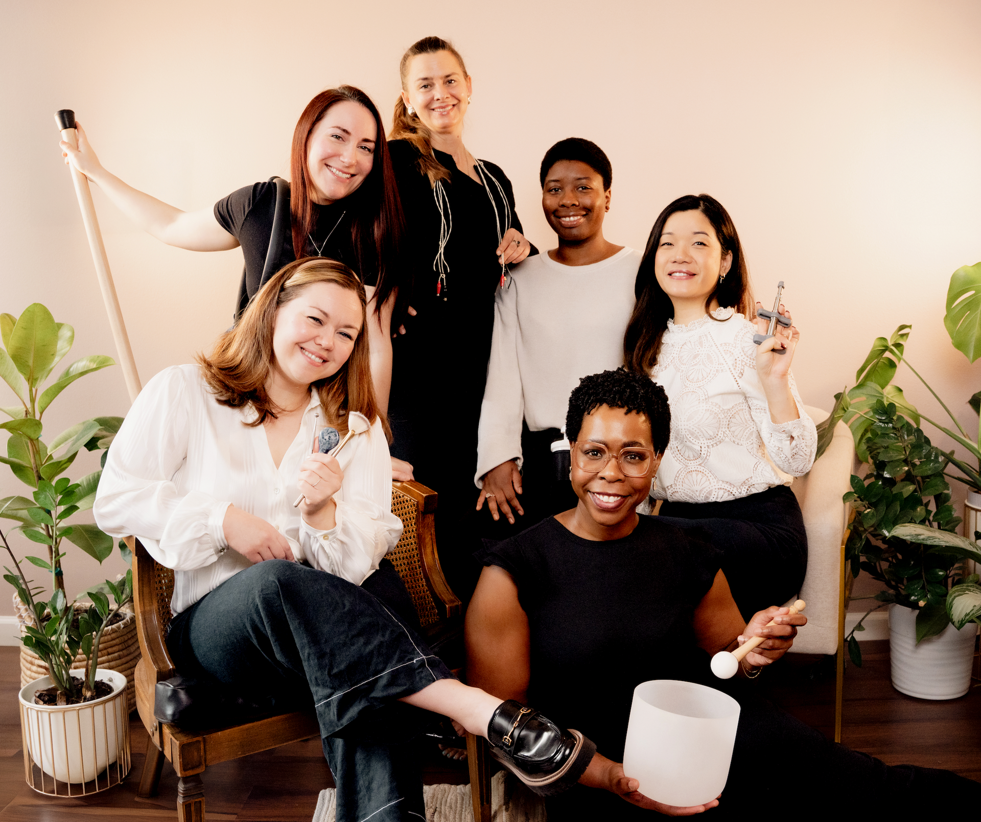 Five people smiling and posing in a cozy indoor living room with plants and warm lighting