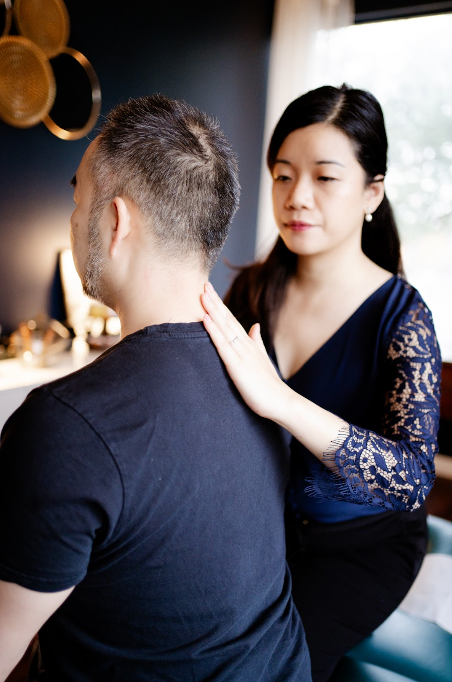 Massage therapist kneads a seated person's shoulders in a softly lit room