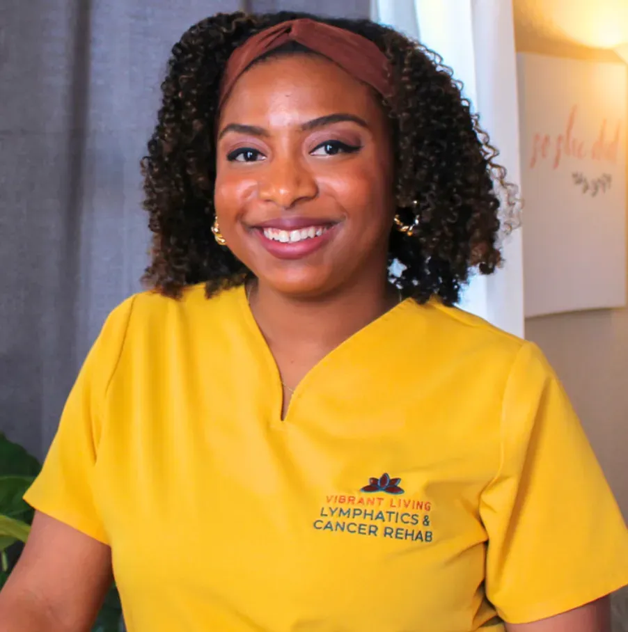 Smiling healthcare worker in yellow scrubs with a red headband, standing indoors.