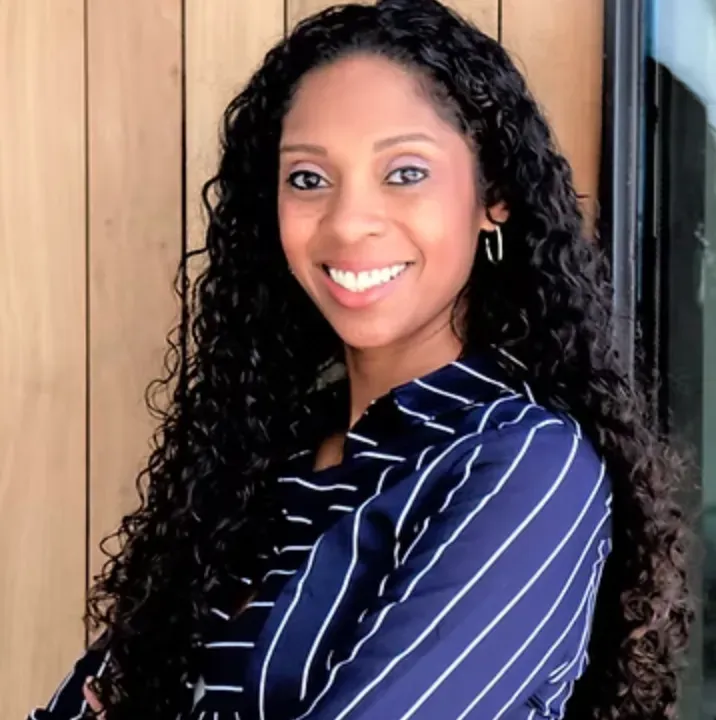 Smiling woman in a navy striped blouse standing indoors by a wooden door