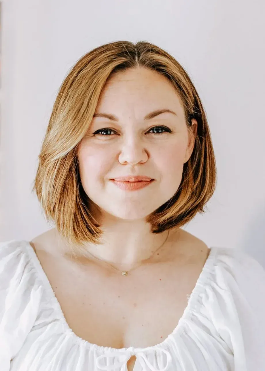Smiling woman with shoulder-length blonde hair wearing a white blouse against a light background