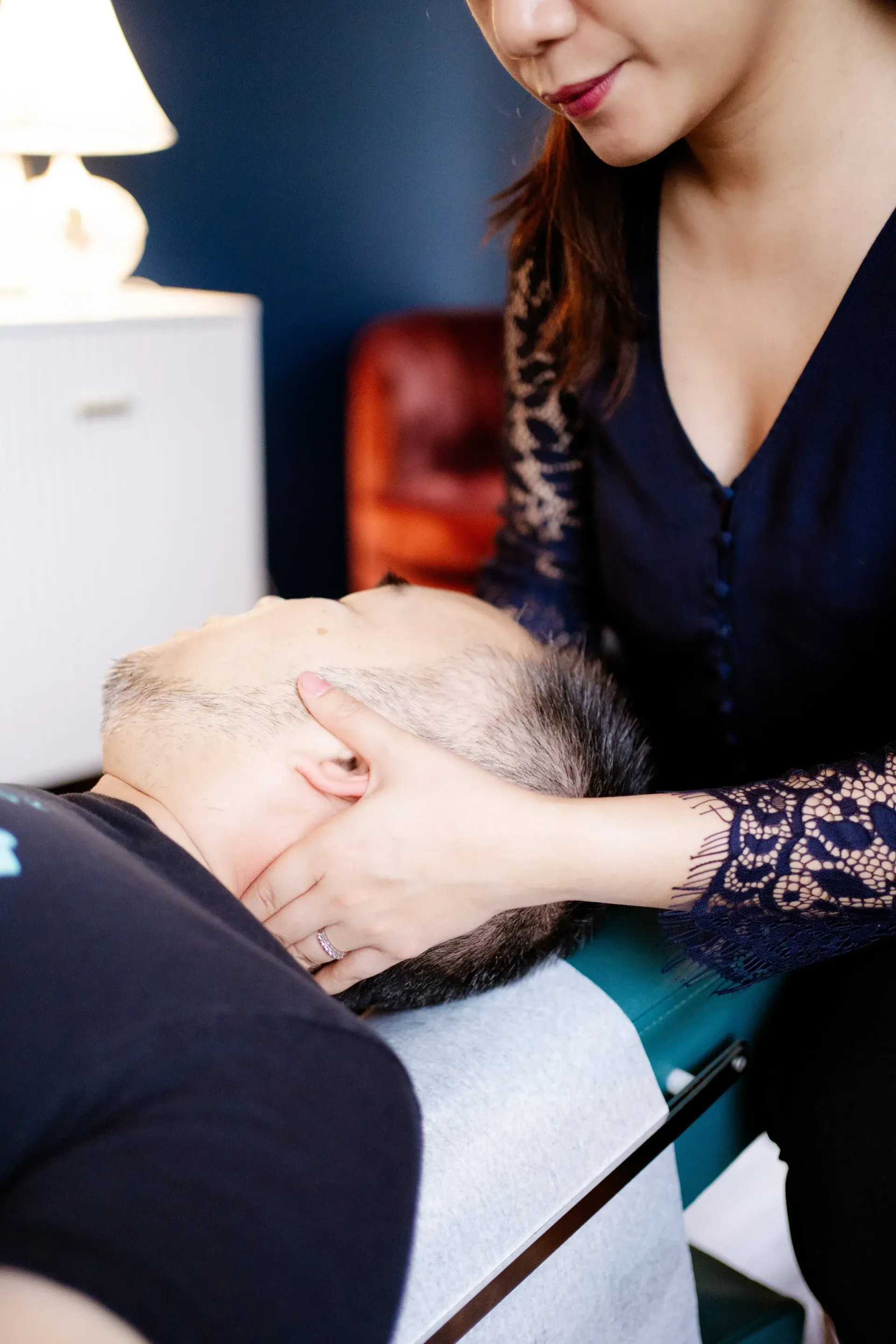 Woman gently holding a bald man’s head during a seated treatment in a clinic room