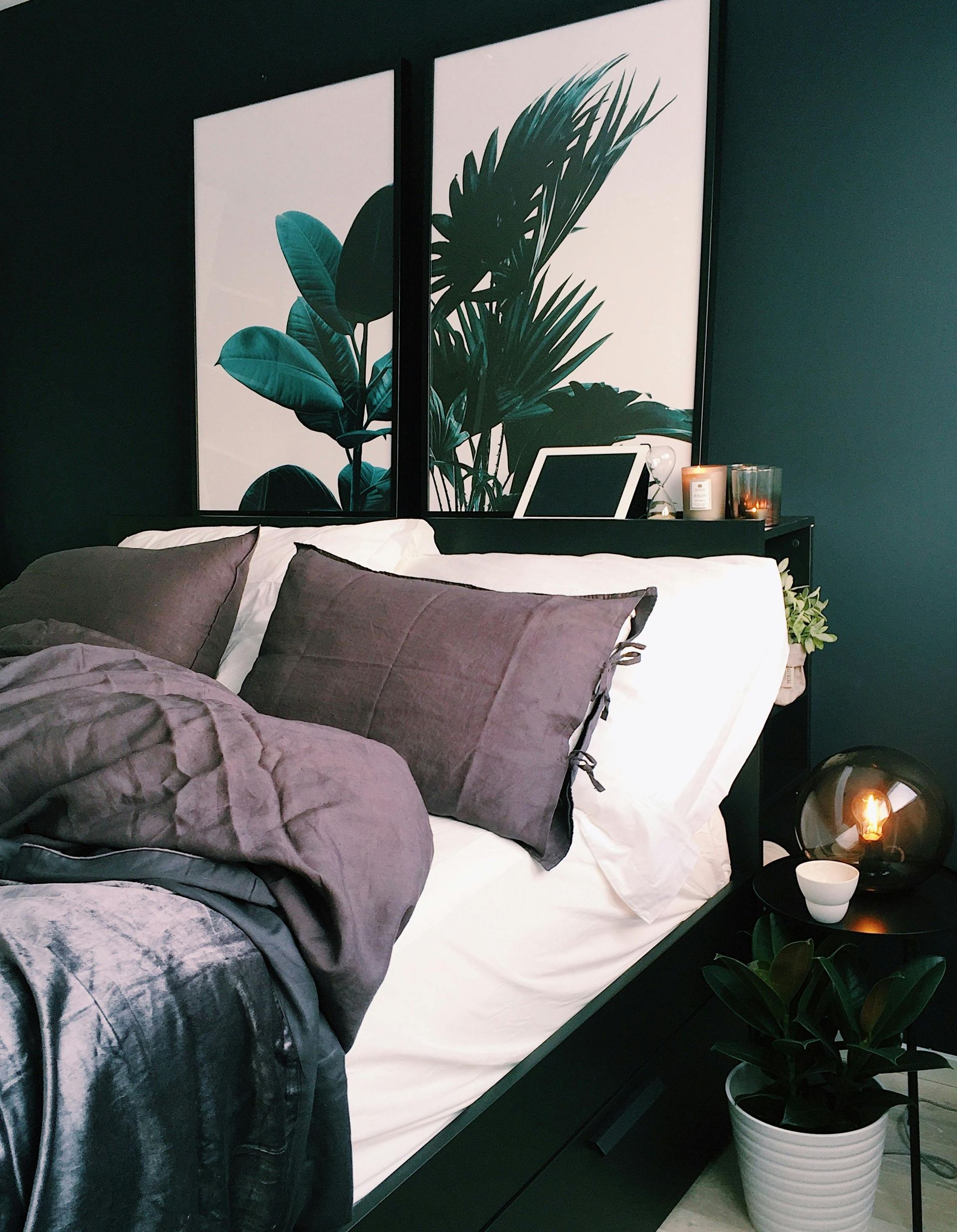 Camera da letto buia e accogliente con letto rifatto, lenzuola grigie e un quadro botanico alle sue spalle.