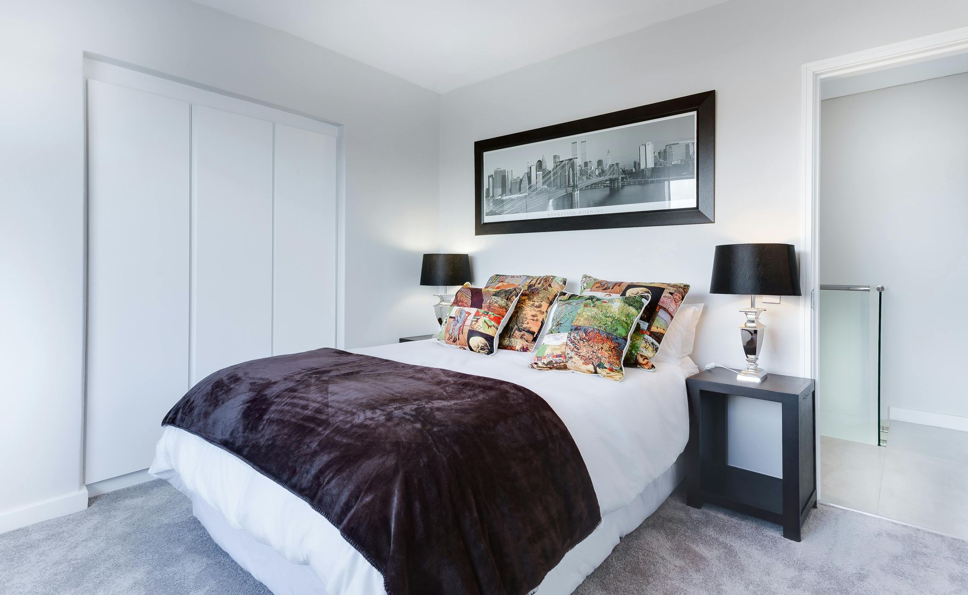 Camera da letto luminosa con letto bianco, coperta scura, cuscini a fantasia e lampade da comodino abbinate.