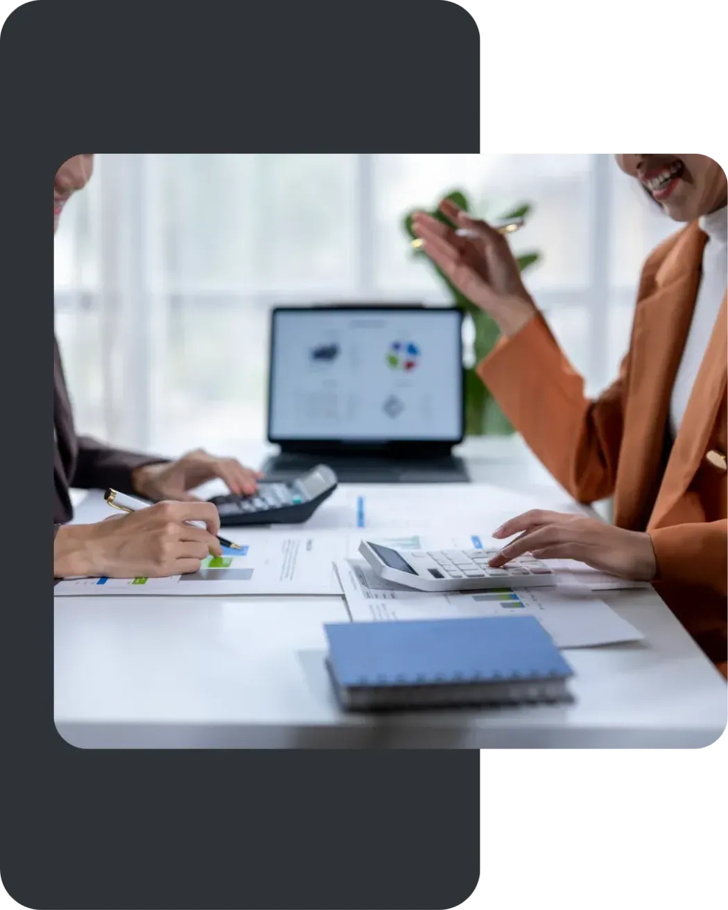 People in a meeting around a laptop and papers at a white desk in a bright office.