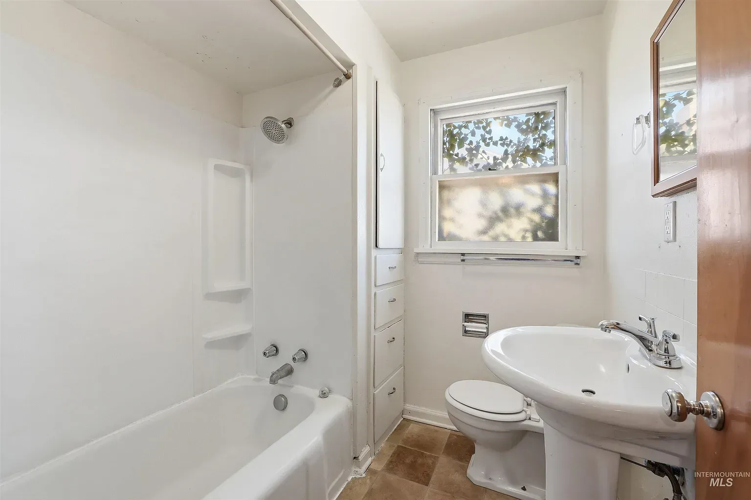 Bright bathroom with white tub, pedestal sink, toilet, and window with frosted lower pane.
