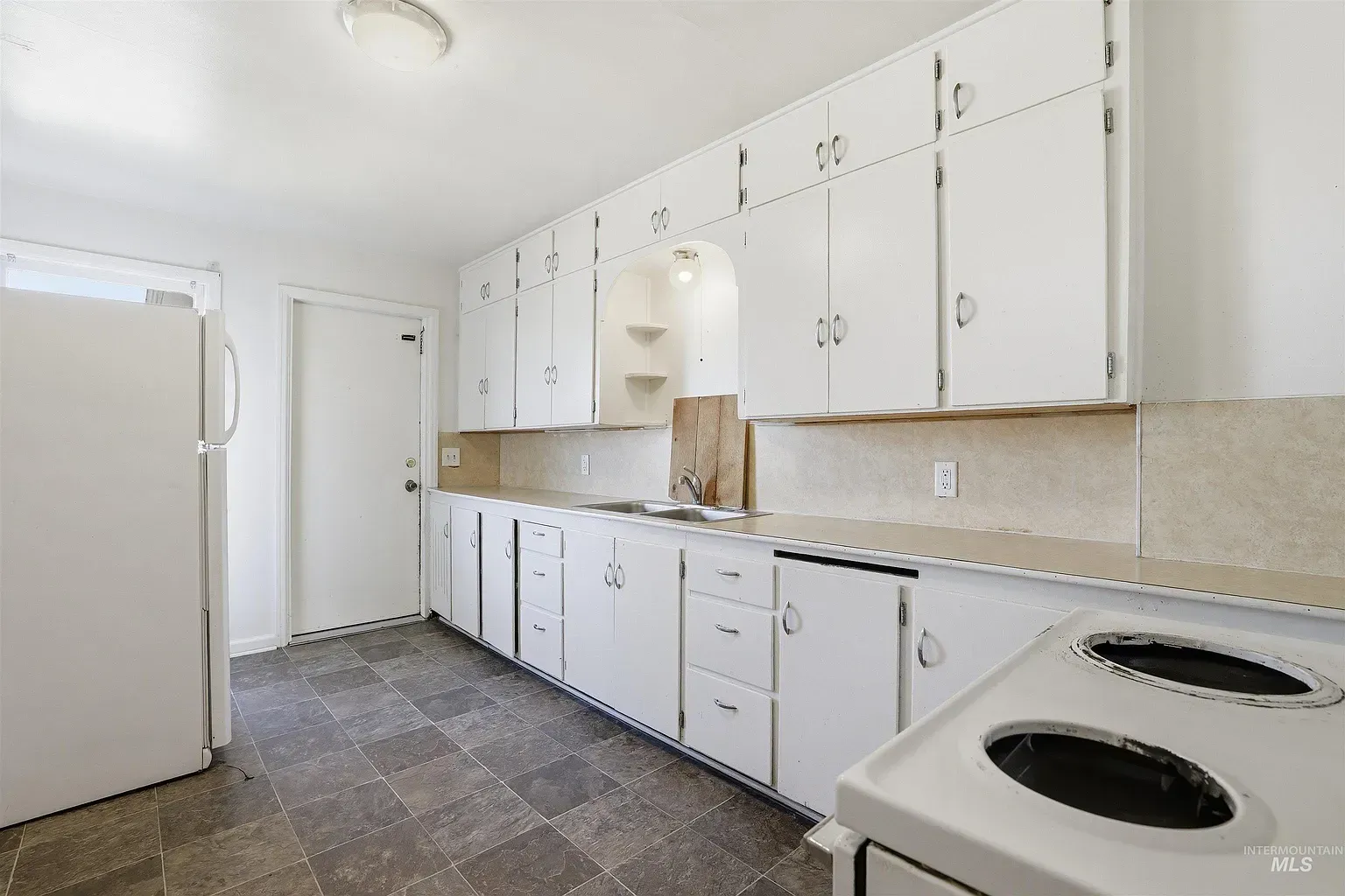 Bright kitchen with white cabinets, beige countertop, white fridge, and black electric stove in a long galley layout
