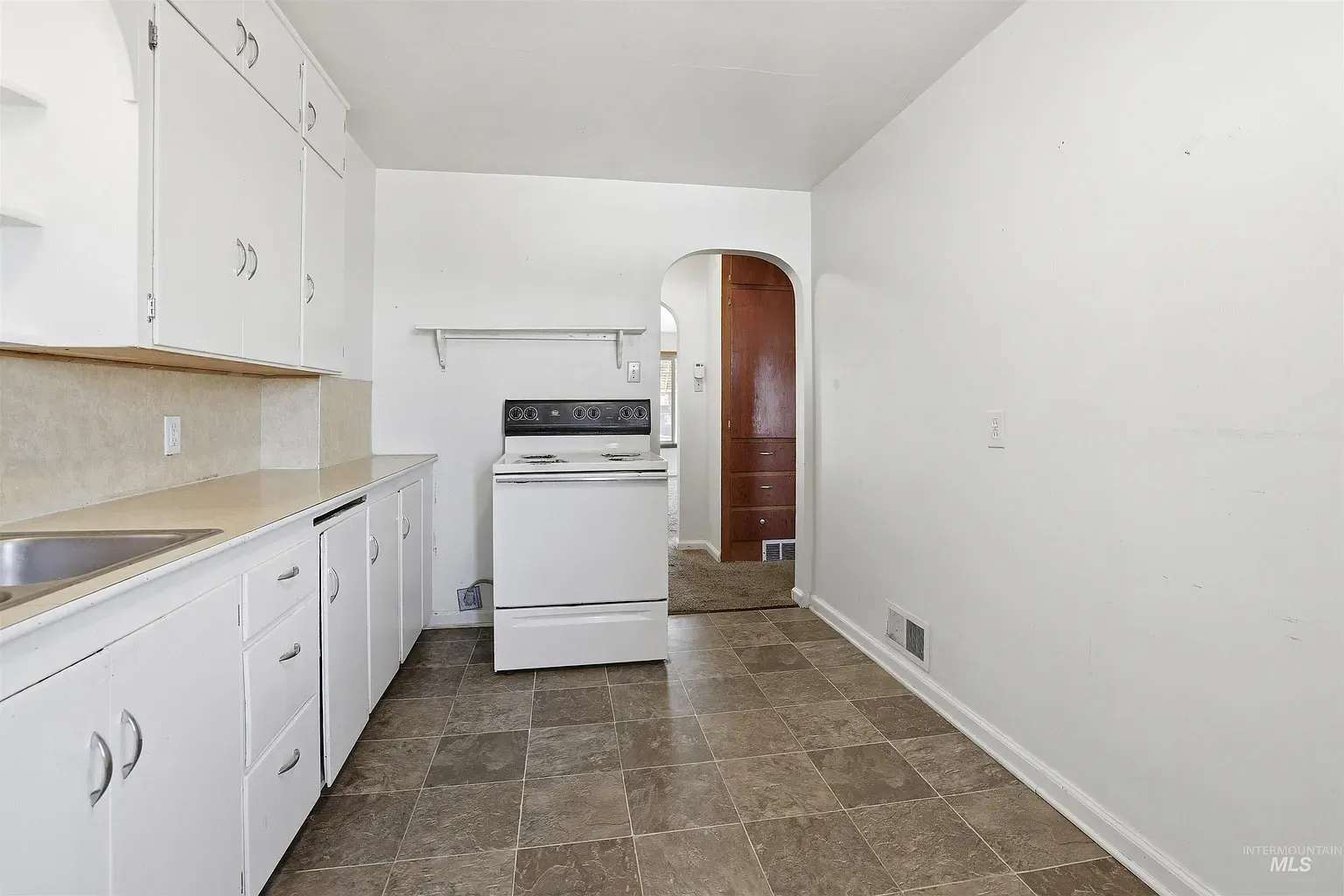 Small white kitchen with cabinets, stove, sink, and tile floor leading to a doorway