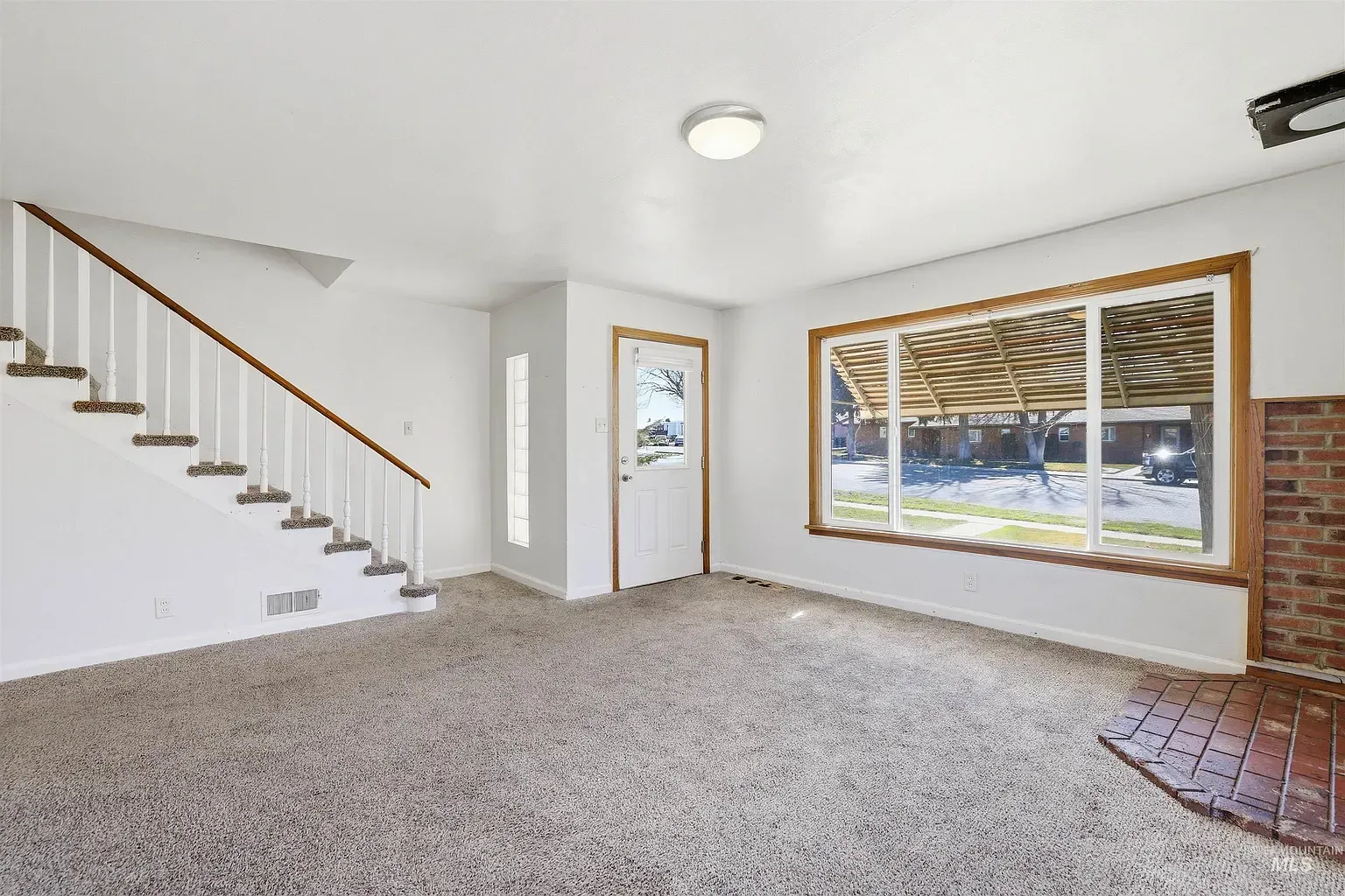 Empty living room with carpet, staircase, and large window with wood blinds