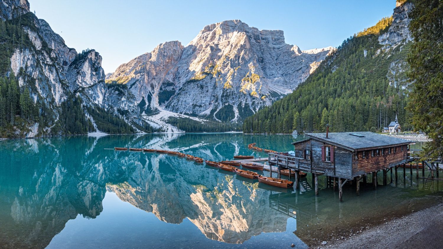 Turquoise mountain lake with snowy peaks reflected in calm water beside a wooden dock and hut