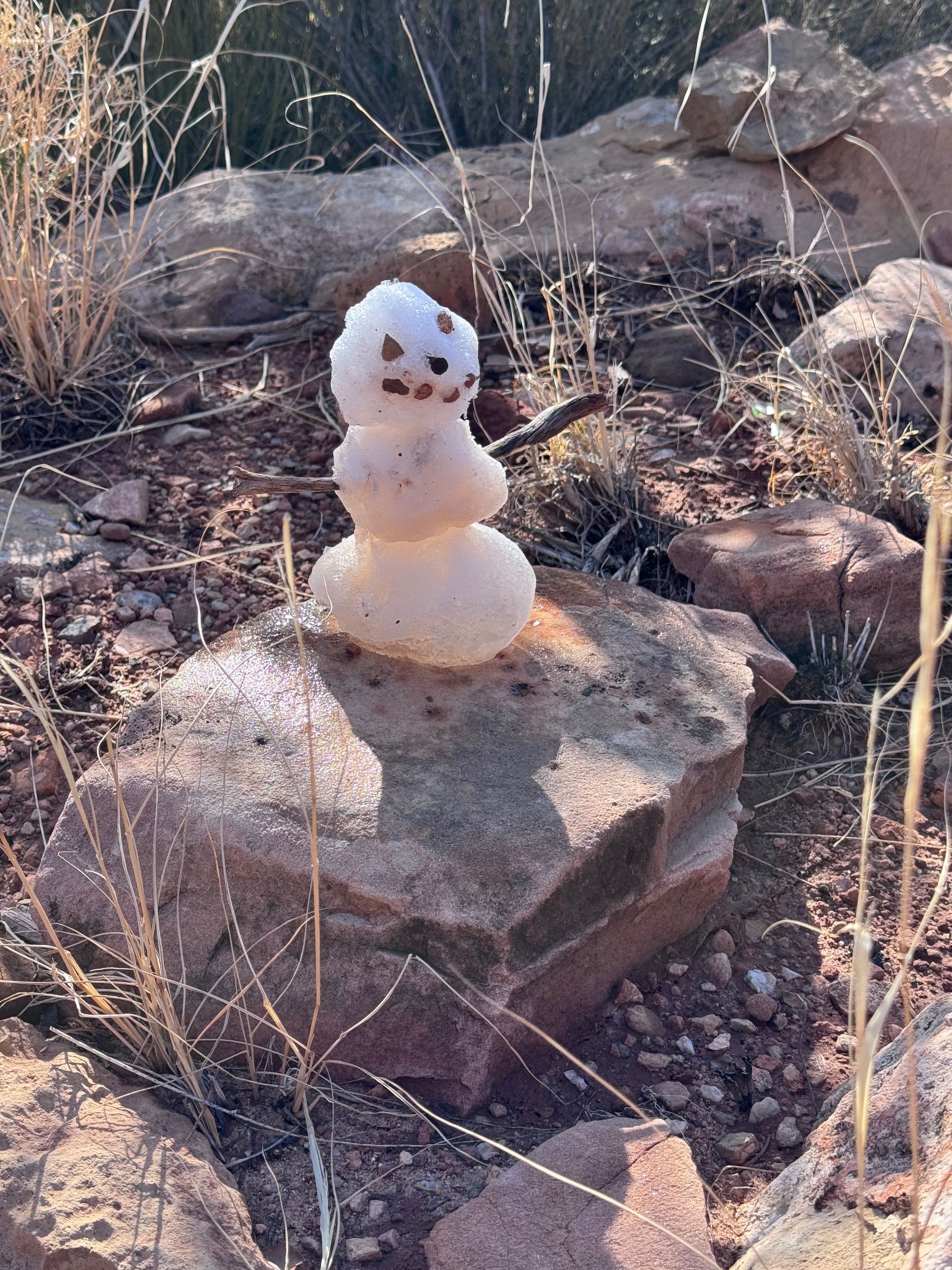 Snowman on a rock in a dry, rocky, outdoor setting.