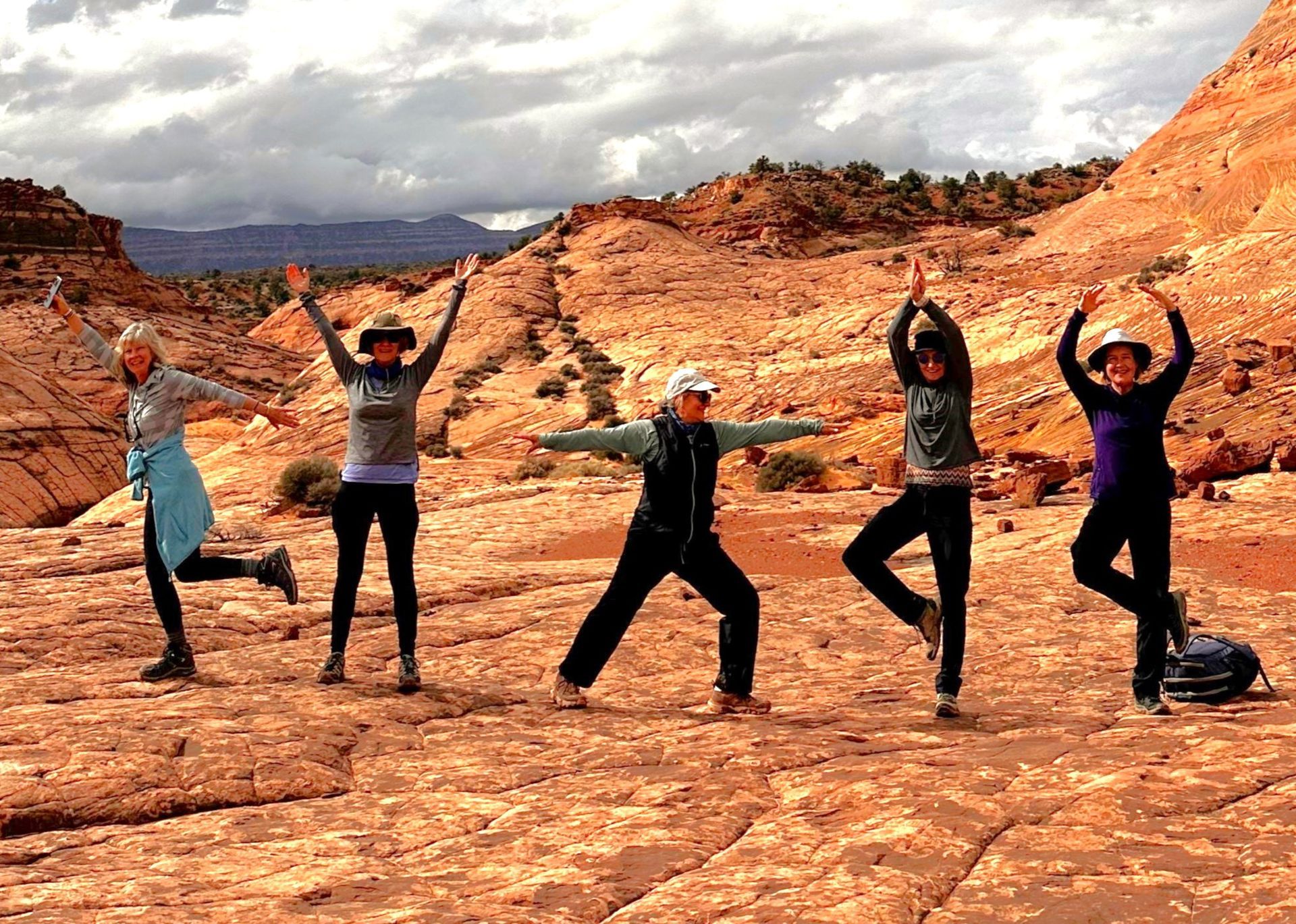 A group of women are doing yoga poses in the desert.